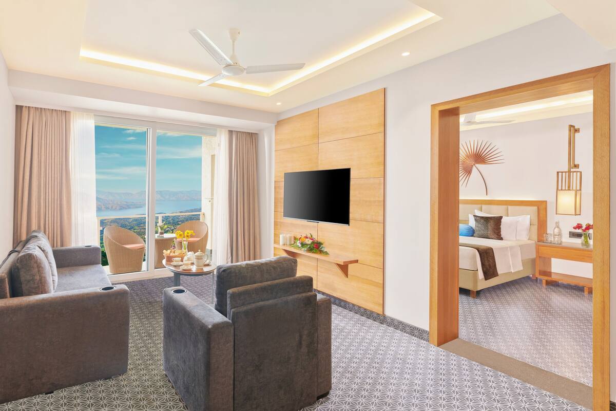 A hotel room with a large TV, a sofa, a coffee table, and a view of the outdoors.