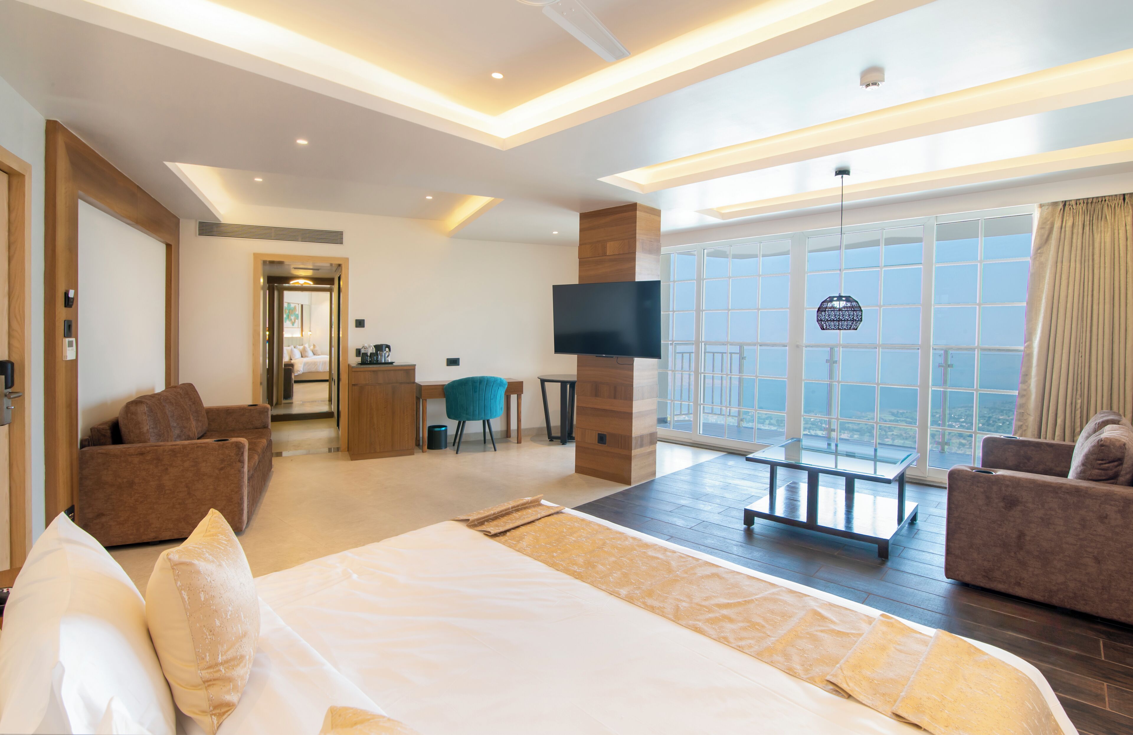 Een moderne hotelkamer met een groot bed, twee banken, een televisie en een balkon met uitzicht op de stad.
