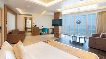 Een moderne hotelkamer met een groot bed, twee banken, een televisie en een balkon met uitzicht op de stad.