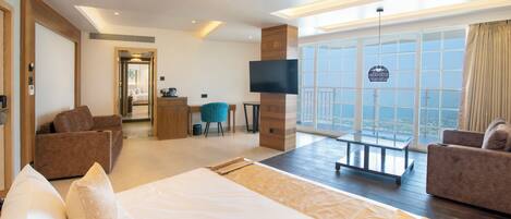 A modern hotel room with a large bed, two sofas, a TV, and a balcony with a city view.