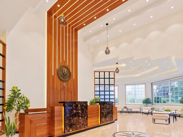 A modern reception area with a wooden reception desk, a decorative wall piece, and a seating area with tables and chairs. - The Cliff by Zuper - Panchgani (Wai)