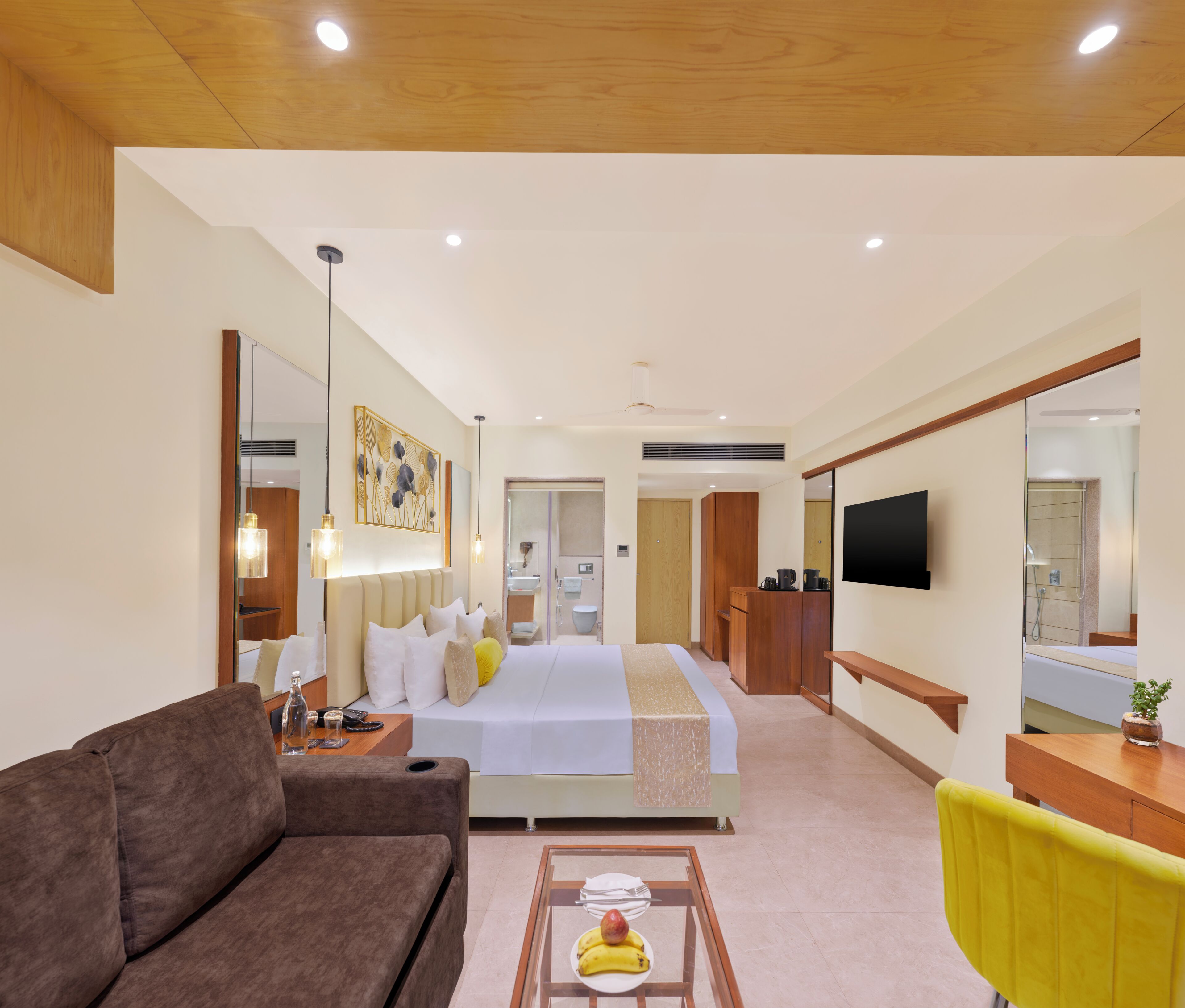 Une chambre d’hôtel avec un lit, un canapé, une télévision, un bureau et une salle de bain visible à travers une porte ouverte.