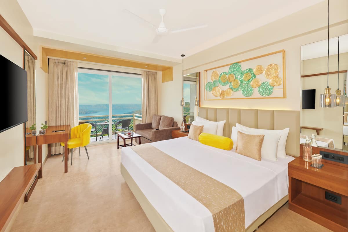 A hotel room with a large bed, a desk with a chair, a TV, and a balcony with a view.