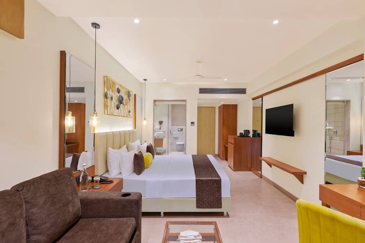 A modern hotel room with a large bed, a sofa, a TV, and a desk.