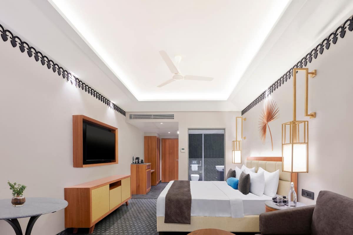 A hotel room with a bed, a sofa, a TV, a desk, and a bathroom visible through an open door.