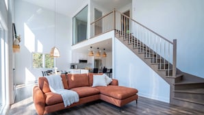 Ein modernes Wohnzimmer mit einem Ecksofa, einer Treppe und einer Küche im Hintergrund.
