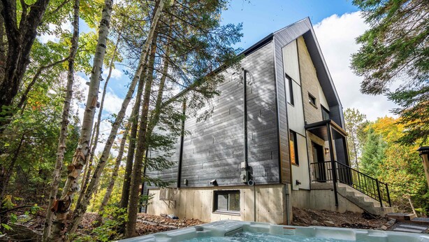 Ein modernes Haus mit Whirlpool in bewaldeter Landschaft.