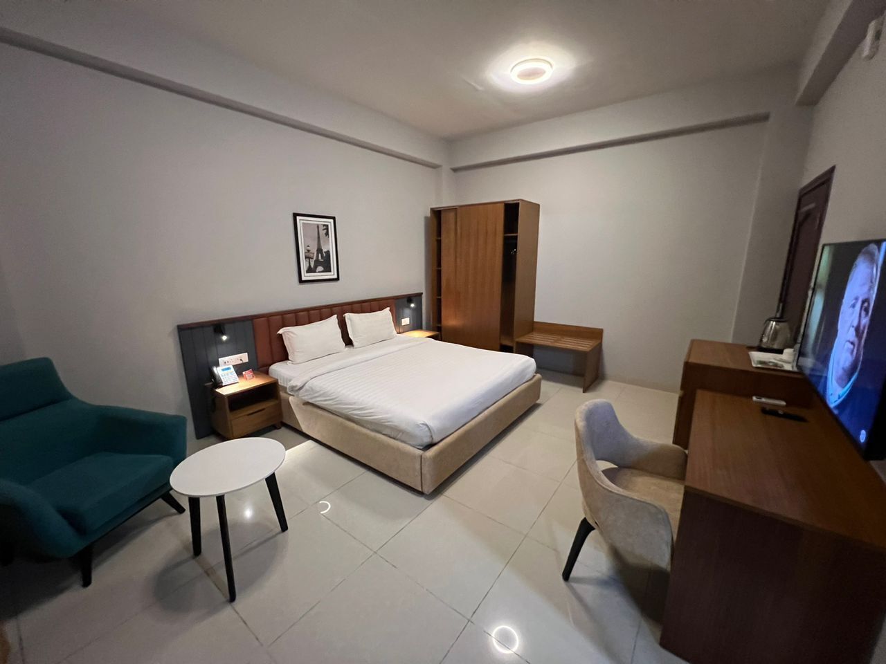 A modern hotel room with a large bed, a desk, a chair, a small table, and a television.