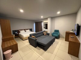 Una habitación de hotel moderna con sofá cama, una cama separada, televisión, escritorio y baño.