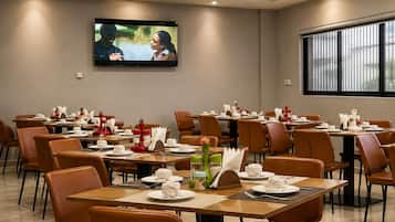 Une salle de conférence avec des tables dressées pour un repas, un téléviseur fixé au mur et une grande fenêtre.