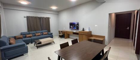 A modern living room with a sofa set, a dining table with chairs, a TV, and a kitchen area.