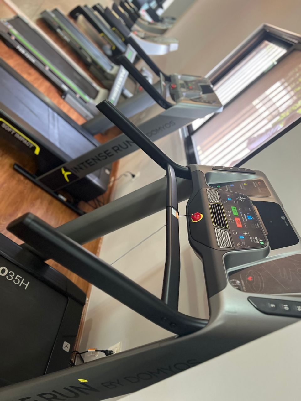 A treadmill with a digital display and control panel, surrounded by other exercise equipment.