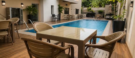 A poolside area with a table and chairs, surrounded by a wooden deck and potted plants.
