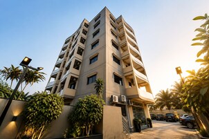 Un edificio residencial de varios pisos con balcones, unidades de aire acondicionado y una entrada protegida por un portón.