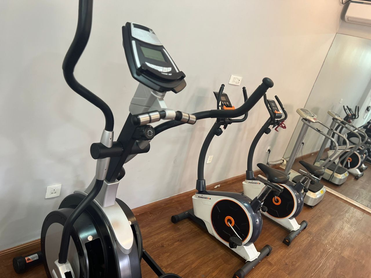 Varias bicicletas estáticas alineadas en una habitación con suelo de madera y pared blanca.