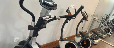 Varias bicicletas estáticas alineadas en una habitación con suelo de madera y pared blanca.