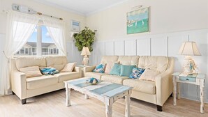 Una sala de estar con dos sofás color crema, una mesa de centro azul y blanca, y una mesita de noche con una lámpara.