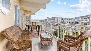 Un balcón con mobiliario de mimbre, una mesa de vidrio y vistas a otros edificios y una calle.