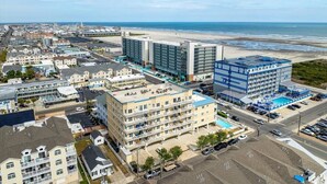 Vista aérea de una zona hotelera costera con varios edificios, incluyendo un hotel grande con piscina y un edificio más pequeño con terraza en la azotea.