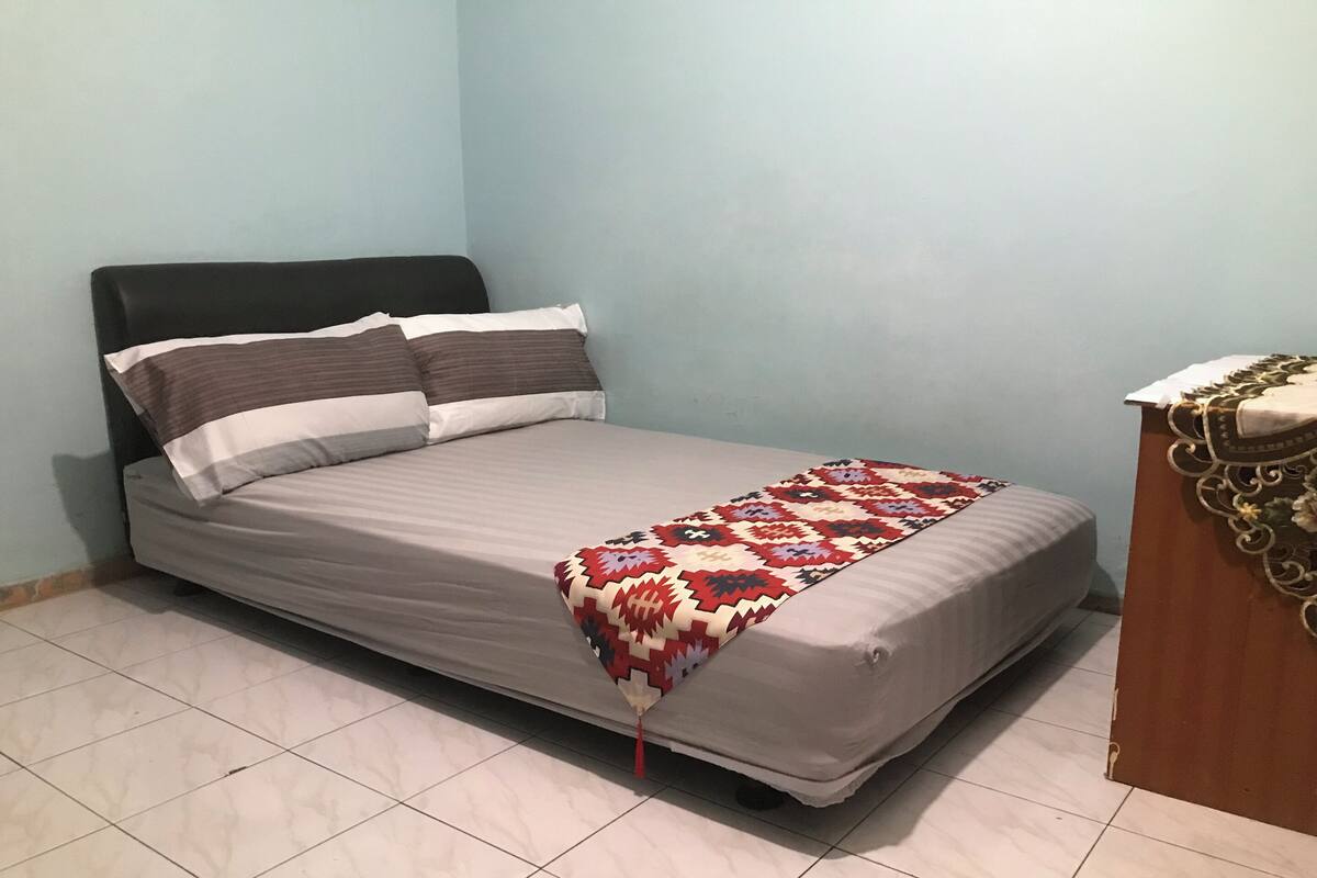 Una cama individual con una colcha estampada, un cabecero y una mesita de noche de madera con un adorno.