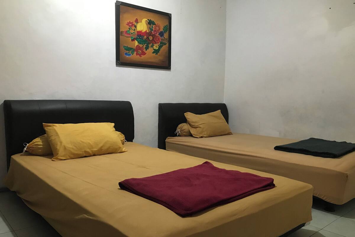 Dos camas individuales con cabeceros negros, ropa de cama color beige y una almohada amarilla en una cama.