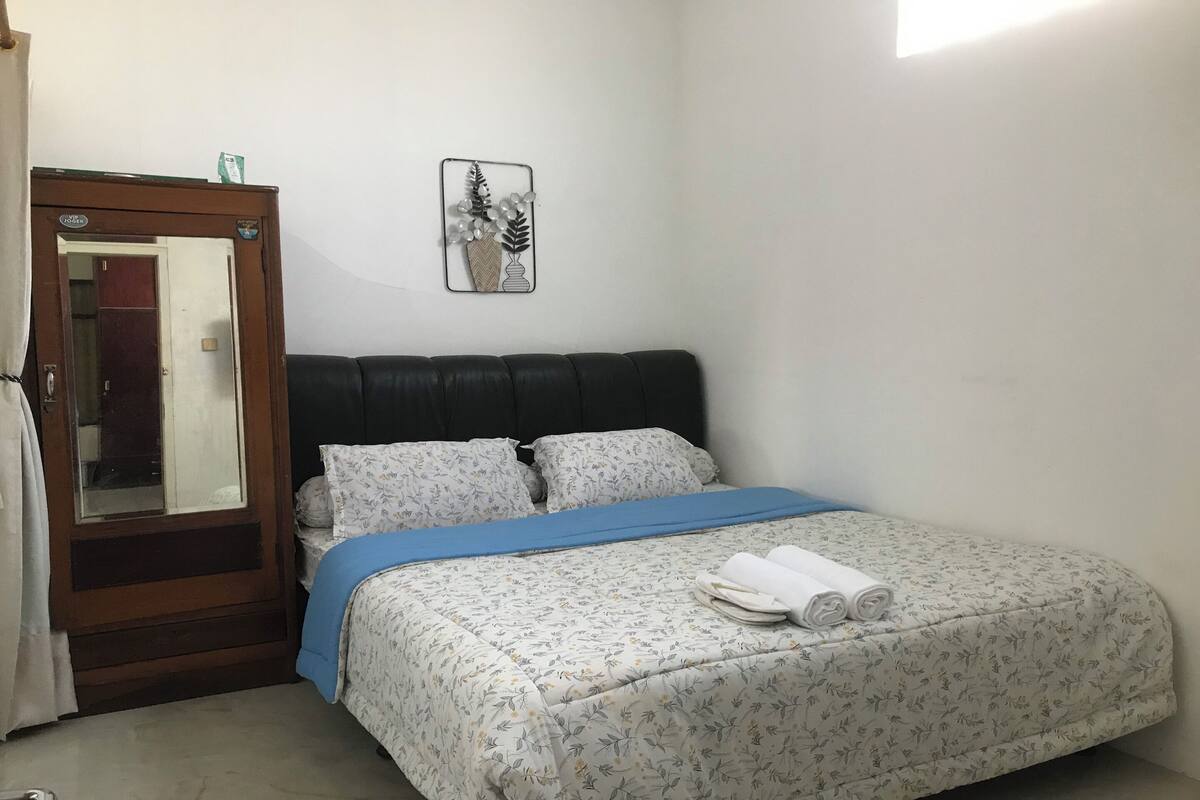 Un dormitorio con una cama, un armario de madera, un espejo e imagen colgada en la pared.
