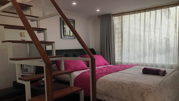 A bedroom with a bed, a staircase, a window with curtains, and a framed picture on the wall. - OYO 94320 Homestay Abah Hank Syariah (Yogyakarta)