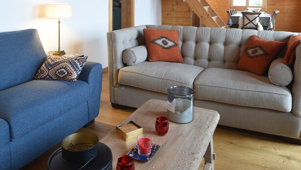 Ein gemütliches Wohnzimmer mit einem blauen Sofa, einem beigen Sofa und einem Holztisch mit Kerzen und einer Lampe.