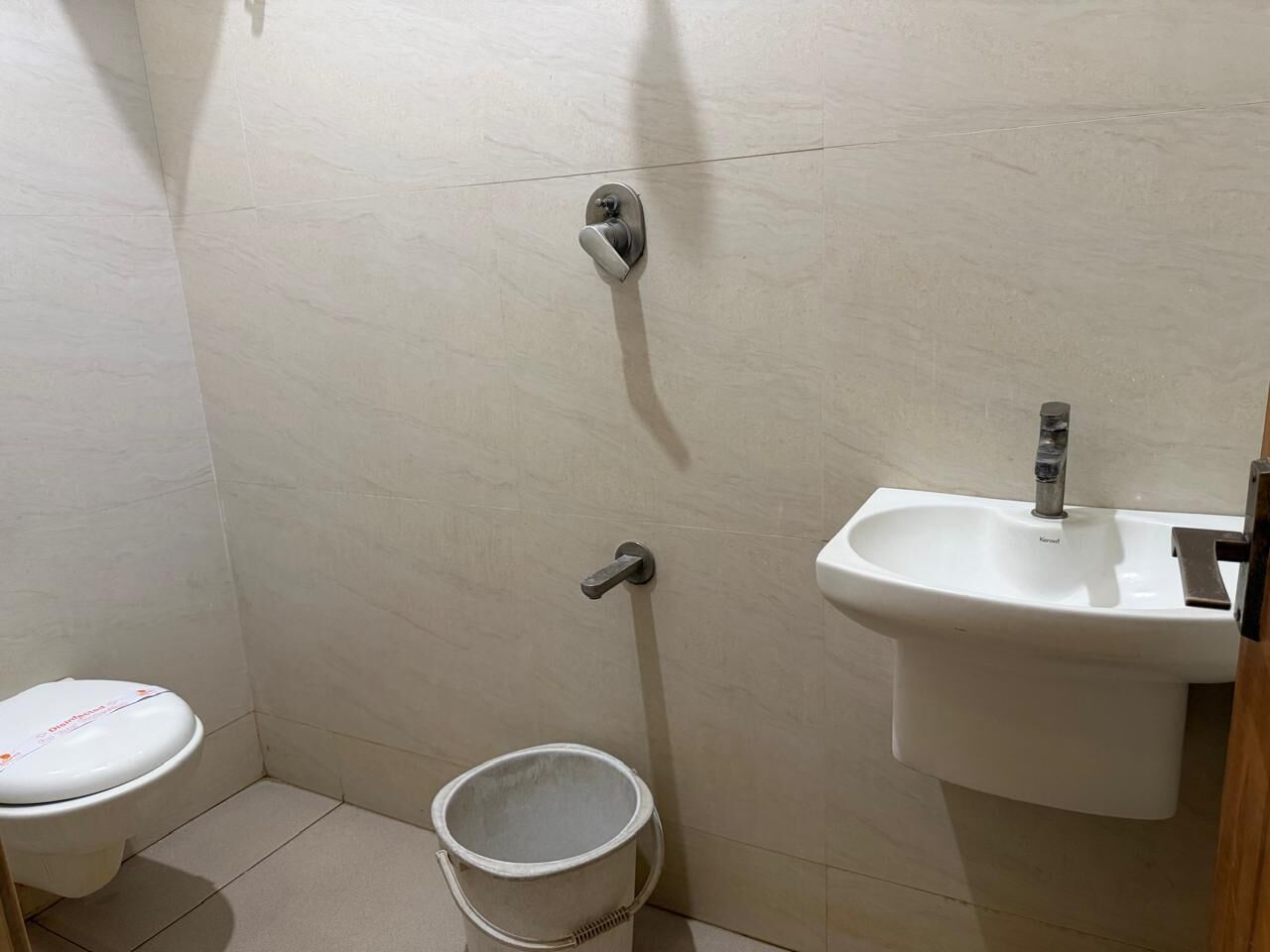 A small bathroom with a toilet, a sink, and a bucket.