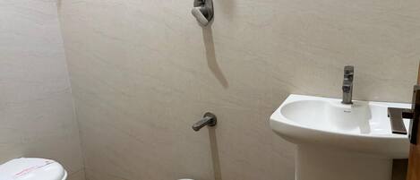 A small bathroom with a toilet, a sink, and a bucket.