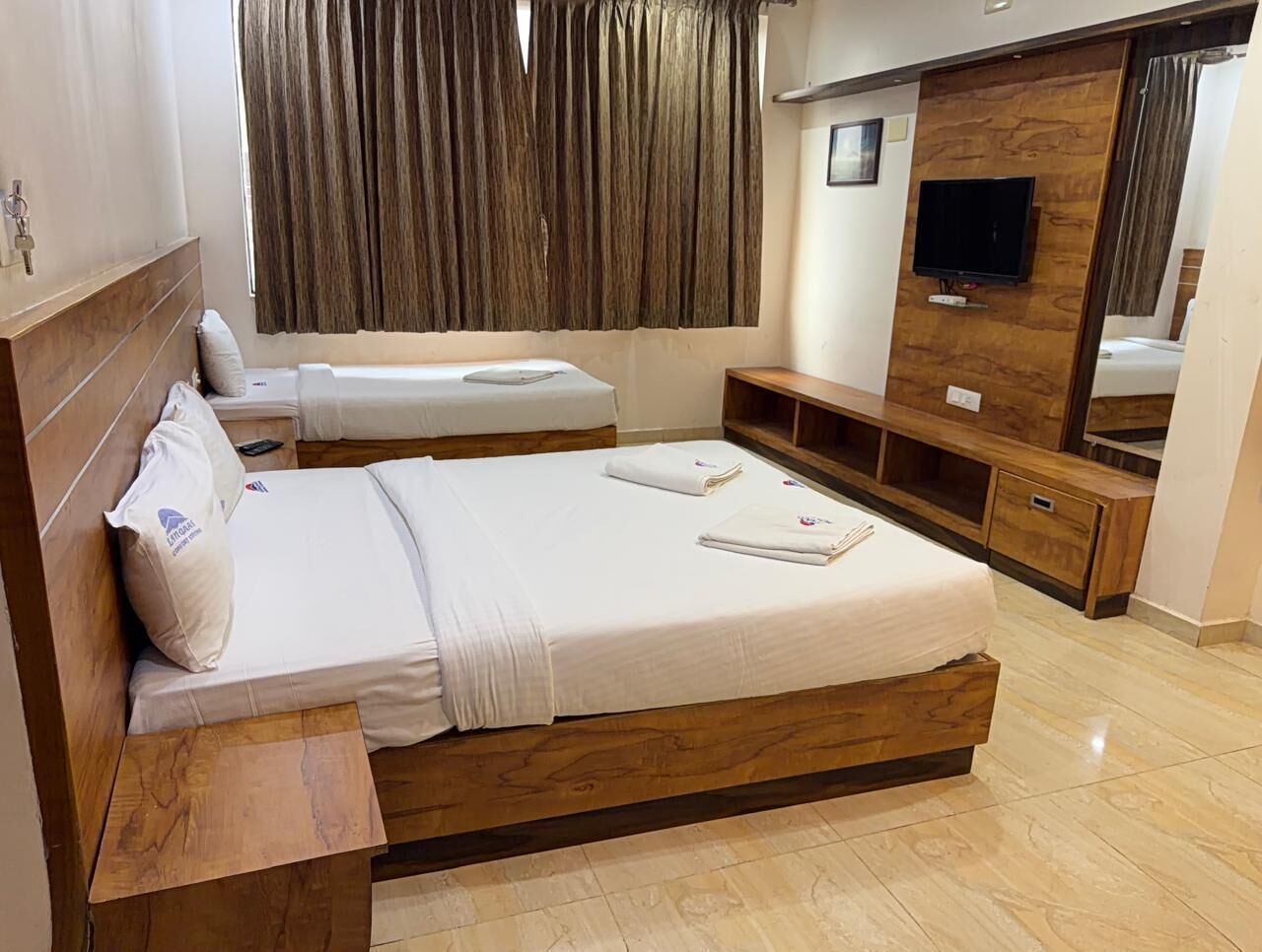Una habitación de hotel con una cama grande, una cama más pequeña, muebles de madera, un televisor y un espejo.