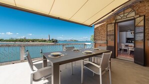 An outdoor dining area with a table set for four, overlooking a body of water with a distant tower. - Ca' delle Contesse   Luxury waterfront apartment (Lido)