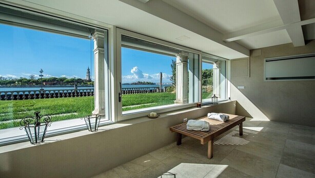 A spacious room with large windows offering a view of a body of water and greenery. - Ca' delle Contesse   Luxury waterfront apartment (Lido)
