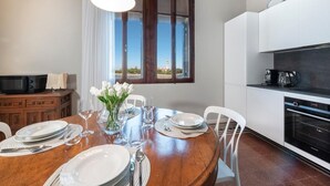 A dining area with a wooden table set for four, a vase of white flowers, and a view of a building through a window. - Ca' delle Contesse   Luxury waterfront apartment (Lido)