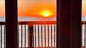A sunset view from a wooden deck with a railing, overlooking the sea.