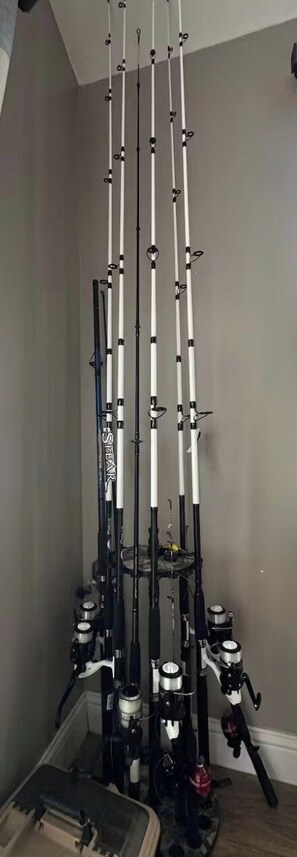 A vertical rack of fishing rods with reels, a fishing net, and a tackle box.
