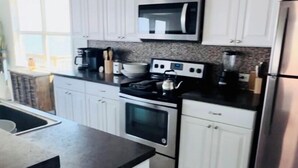 A modern kitchen with white cabinets, a stainless steel refrigerator, a microwave, and a stove.