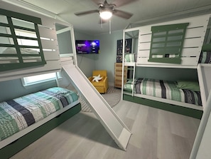 A room with bunk beds, a desk, a chair, and a television.