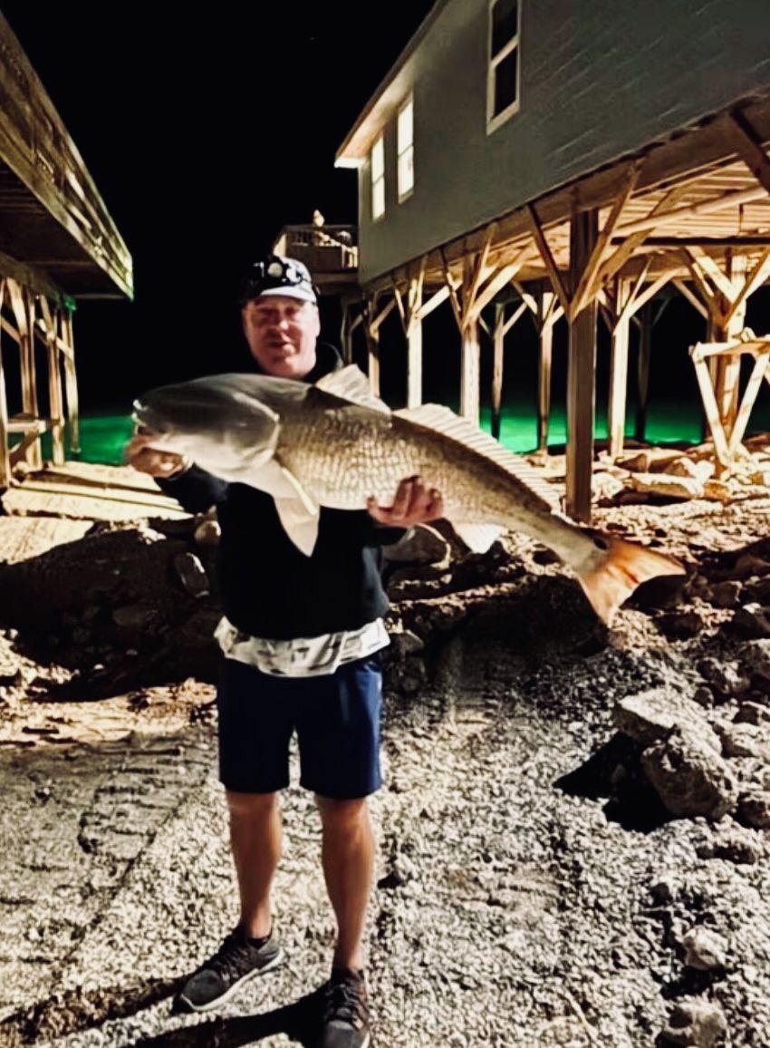 A person holding a large fish in front of a building with a wooden structure.