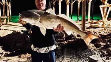 A person holding a large fish in front of a building with a wooden structure.