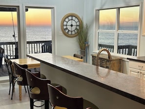 Une cuisine avec un coin bar, une horloge au mur et une vue sur la mer grâce à de grandes fenêtres.