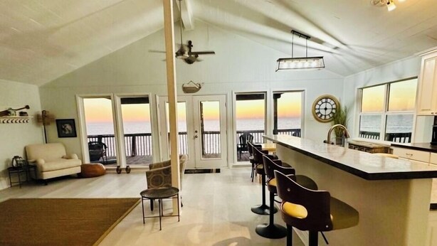 A spacious living area with a balcony overlooking the sea, a kitchen with a bar, and a dining area with bar stools.