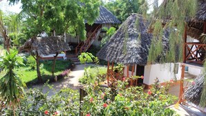 A courtyard with thatched-roof structures, surrounded by lush greenery and flowering plants. - The Tropinest  (Nungwi)