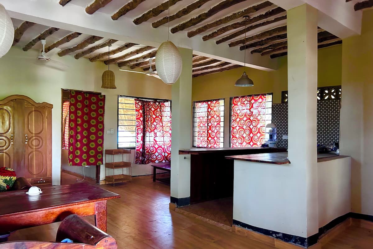 A spacious room with a wooden ceiling, a dining area with a wooden table and chairs, and a kitchen area with a counter and hanging lights.
