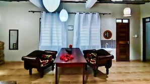 A dining area with a wooden table, two chairs, and a hanging light fixture. - The Tropinest  (Nungwi)