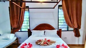 A neatly made bed with a towel and flowers, a wooden headboard, and a window with curtains. - The Tropinest  (Nungwi)