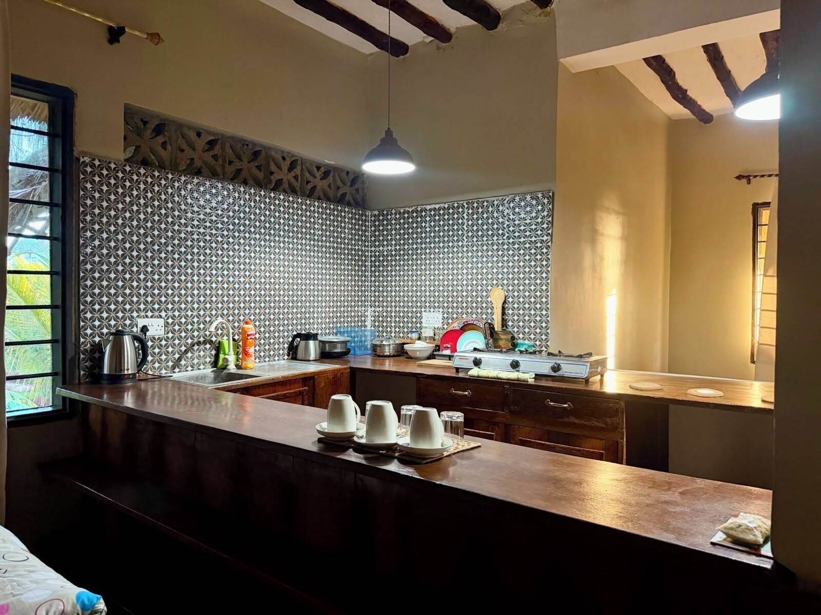 A kitchen with a patterned backsplash, wooden cabinets, and a central island with white plates and cups.