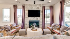 A living room with a stone fireplace, a ceiling fan, and a large TV.