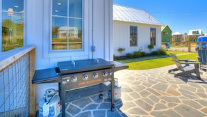 A barbecue grill with propane tanks, a stone patio, and a view of a residential area with houses.