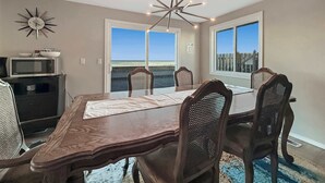 A dining room with a large table, six chairs, a chandelier, a microwave, and a decorative clock. - Dungeness Waterfront, Hot tub, Fire Pit, Pets OK (Sequim)